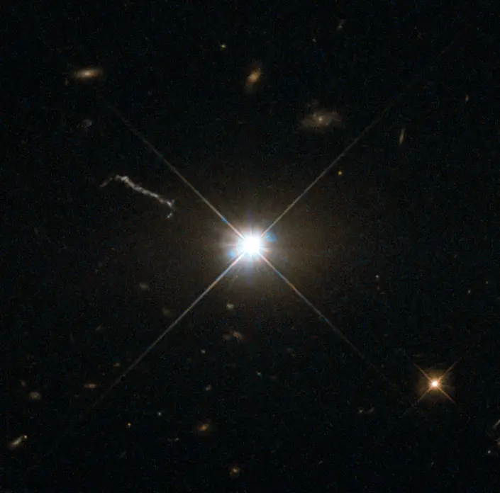 The quasar 3C 273 as a brilliant star-like point with its narrow jet extending to one side, the host galaxy suppressed by a coronagraph.