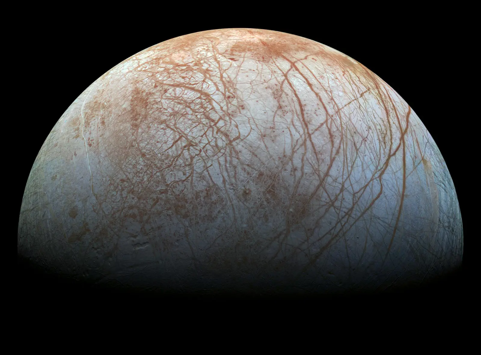 Jupiter's moon Europa filling the frame against black space: a pale blue-white ice world crazed all over with long rust-coloured cracks.