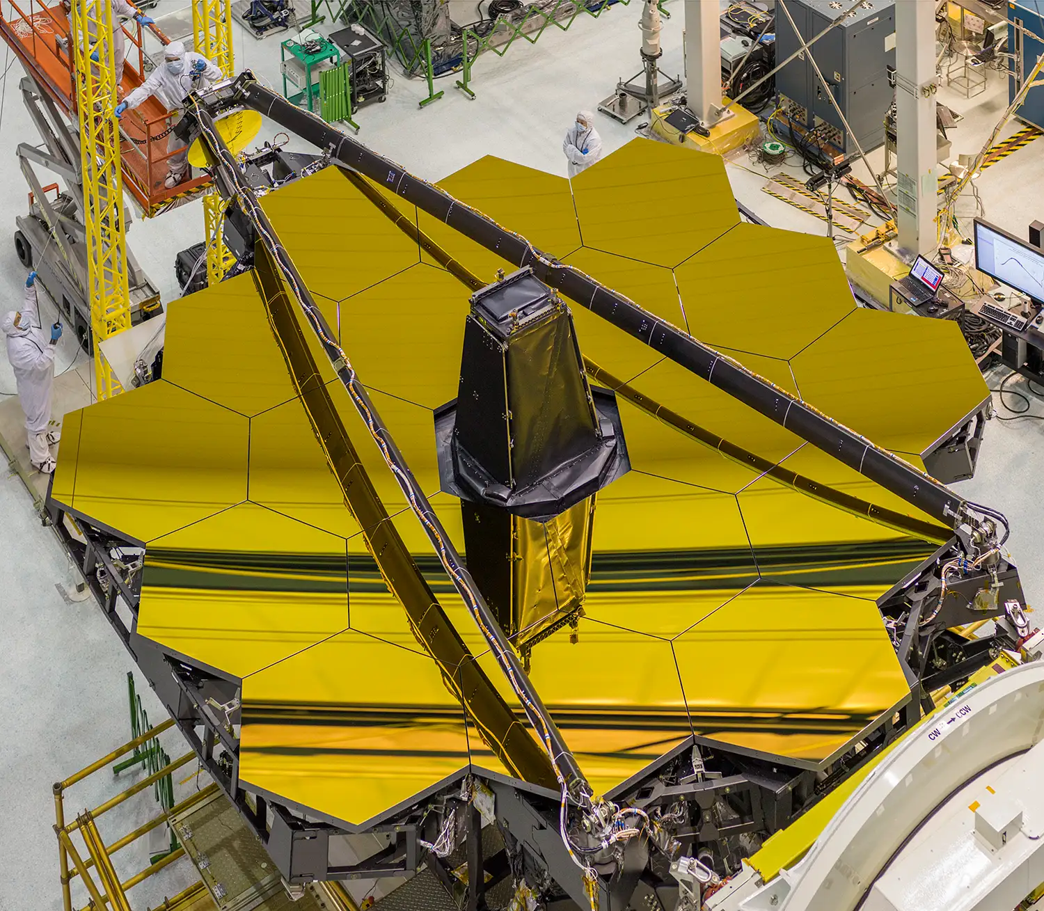 Overhead view of the James Webb Space Telescope in the Goddard clean room: eighteen gold-coated hexagonal mirror segments assembled into one honeycomb, with the black secondary-mirror booms folded across them.