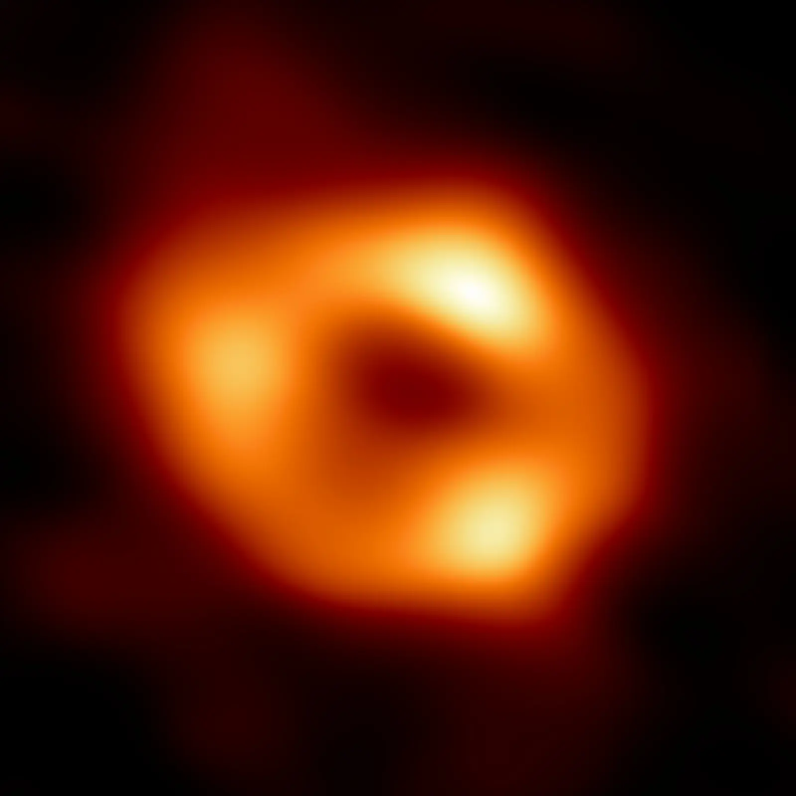 The first image of Sagittarius A*, the Milky Way’s central black hole: a bright uneven orange ring around a dark central shadow.