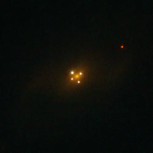 The Einstein Cross: four bright points of light arranged in a cross around the faint diffuse core of a foreground galaxy — four lensed images of a single distant quasar.