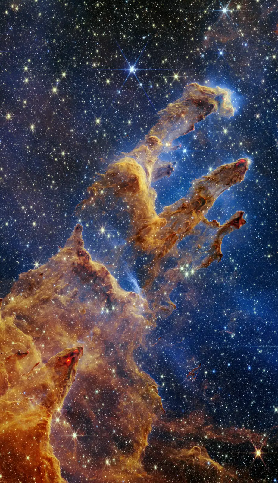 Webb’s full view of the Pillars of Creation: towering rust-and-gold columns of dust rising against a haze of newborn stars.