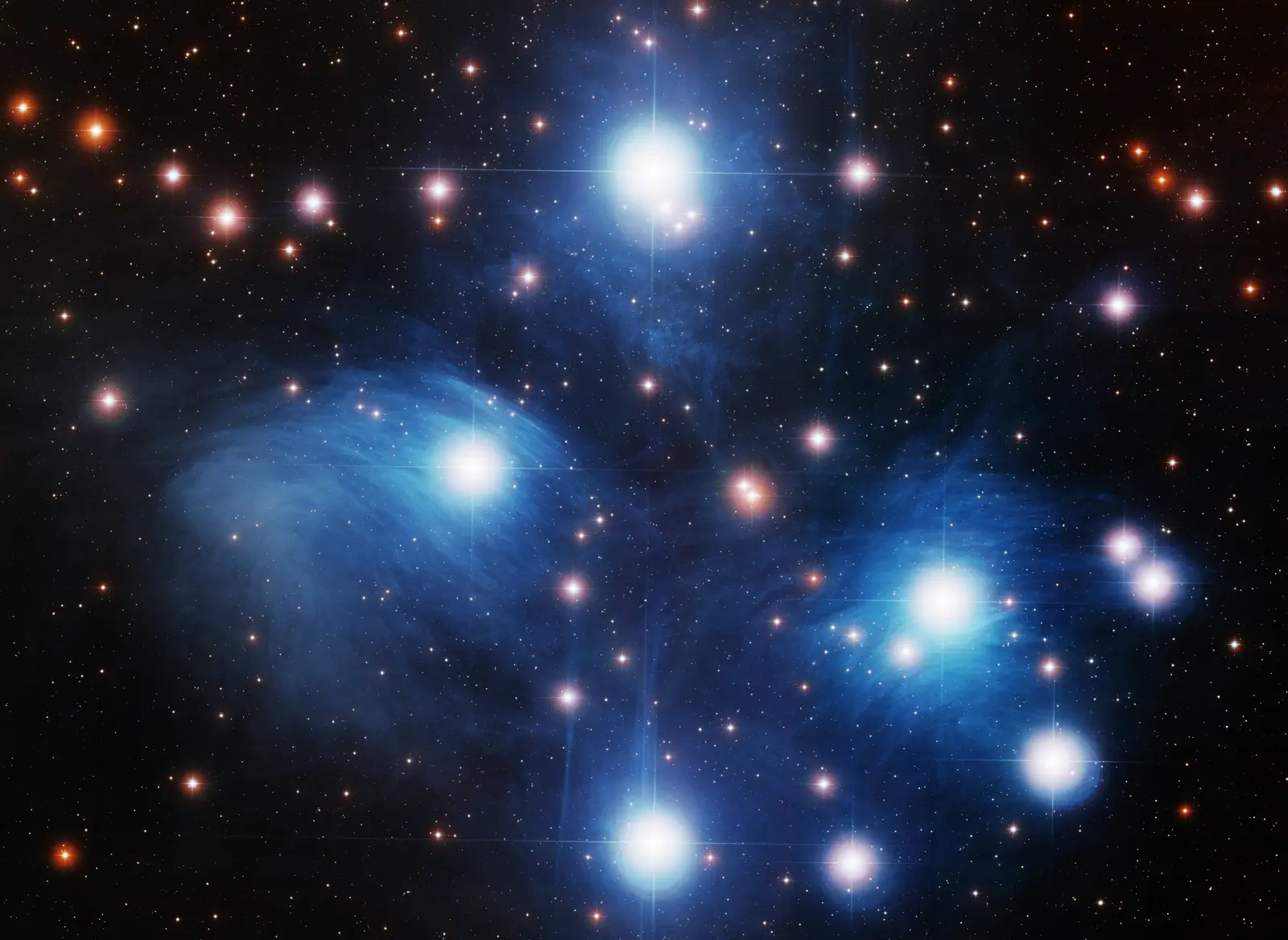 The Pleiades: a tight knot of hot blue-white stars wrapped in wispy blue reflection nebulosity.