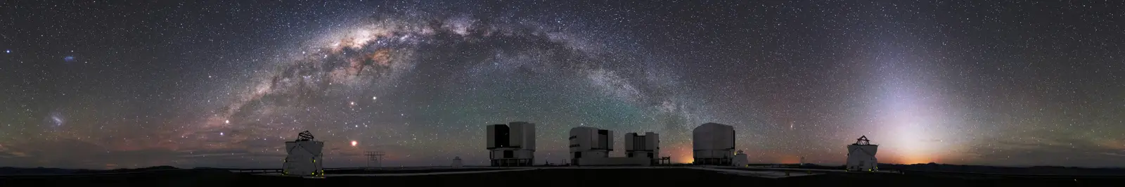 A wide panorama of the Milky Way arching over the Very Large Telescope platform at Paranal, the galactic band running from horizon to horizon.